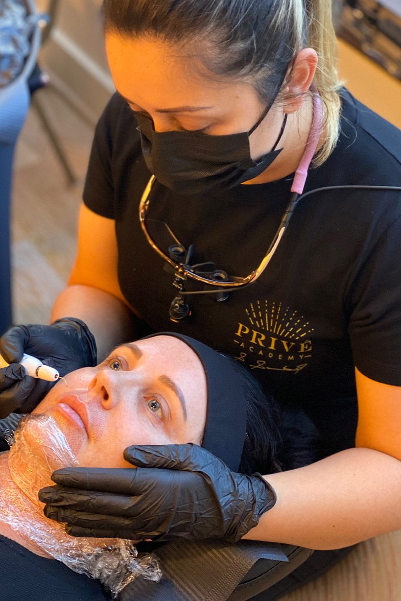 A practitioner treating a model's face with a plasma pen during a Privé live training