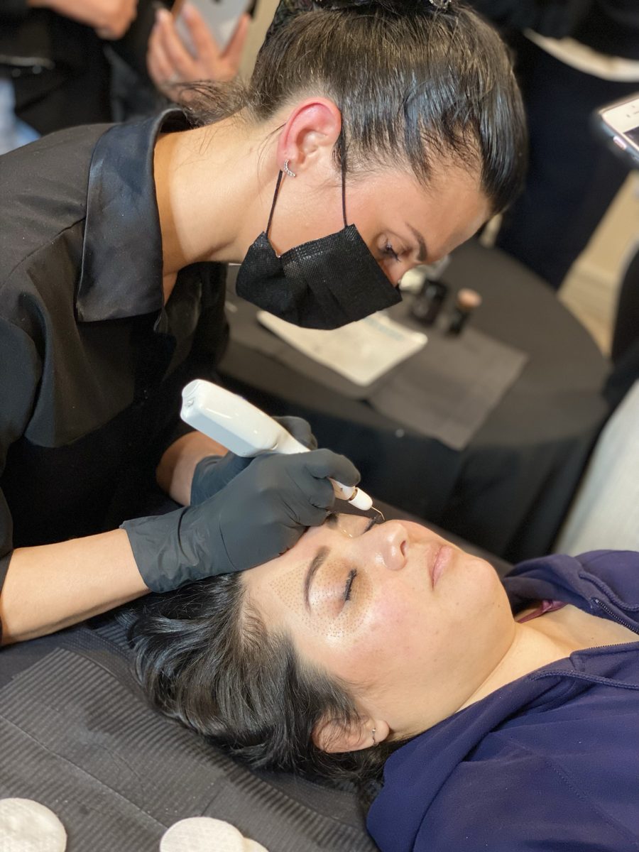 A student treating a model's brow area with a plasma pen while others watch
